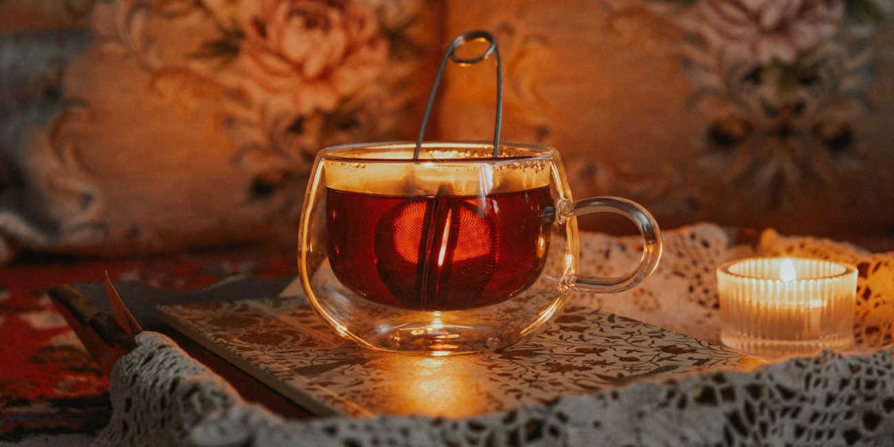 Glas Tasse mit dunklem Tee und Kerzenlicht in gemütlicher Winteratmosphäre.