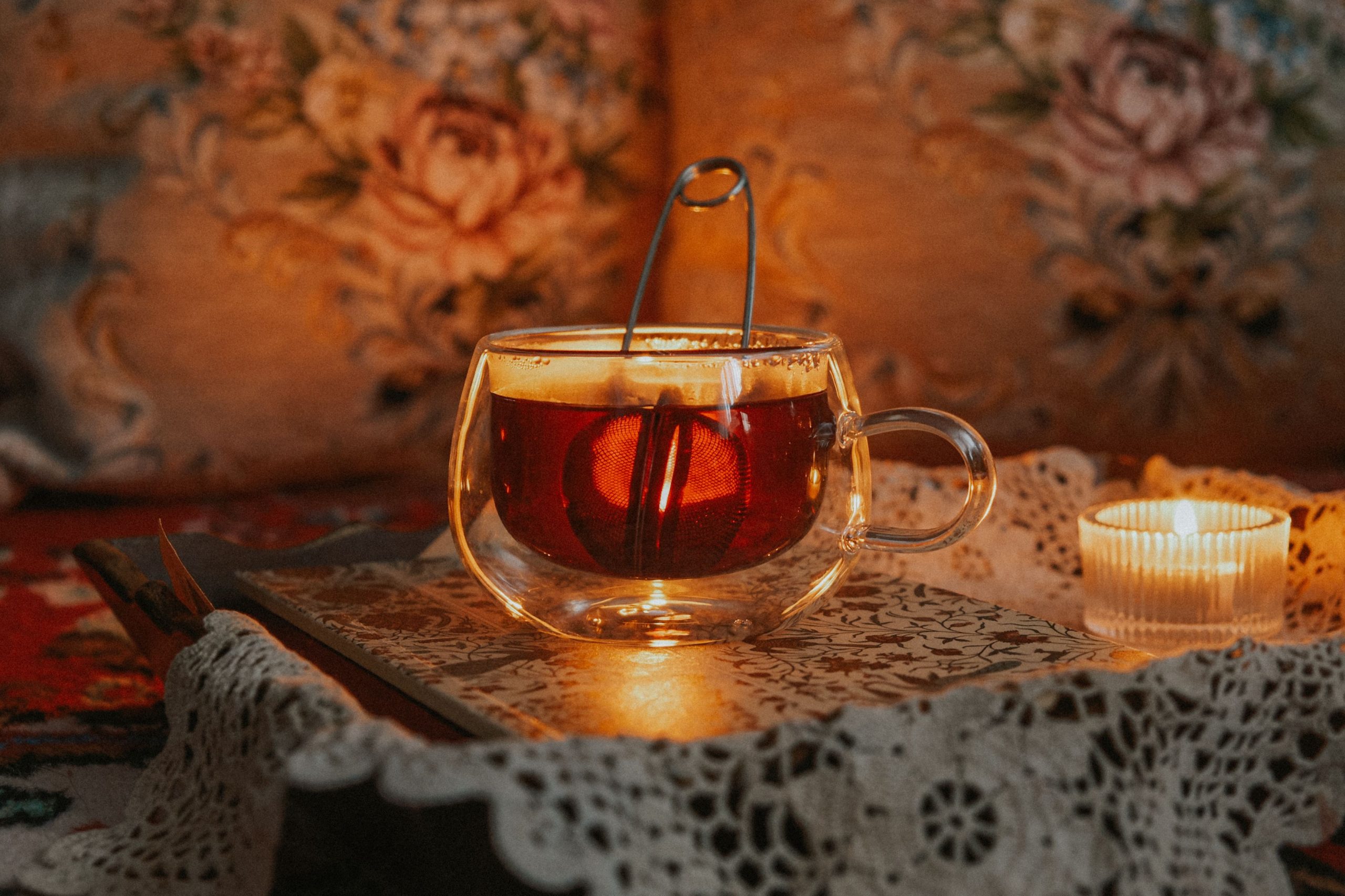 Glas Tasse mit dunklem Tee und Kerzenlicht in gemütlicher Winteratmosphäre.