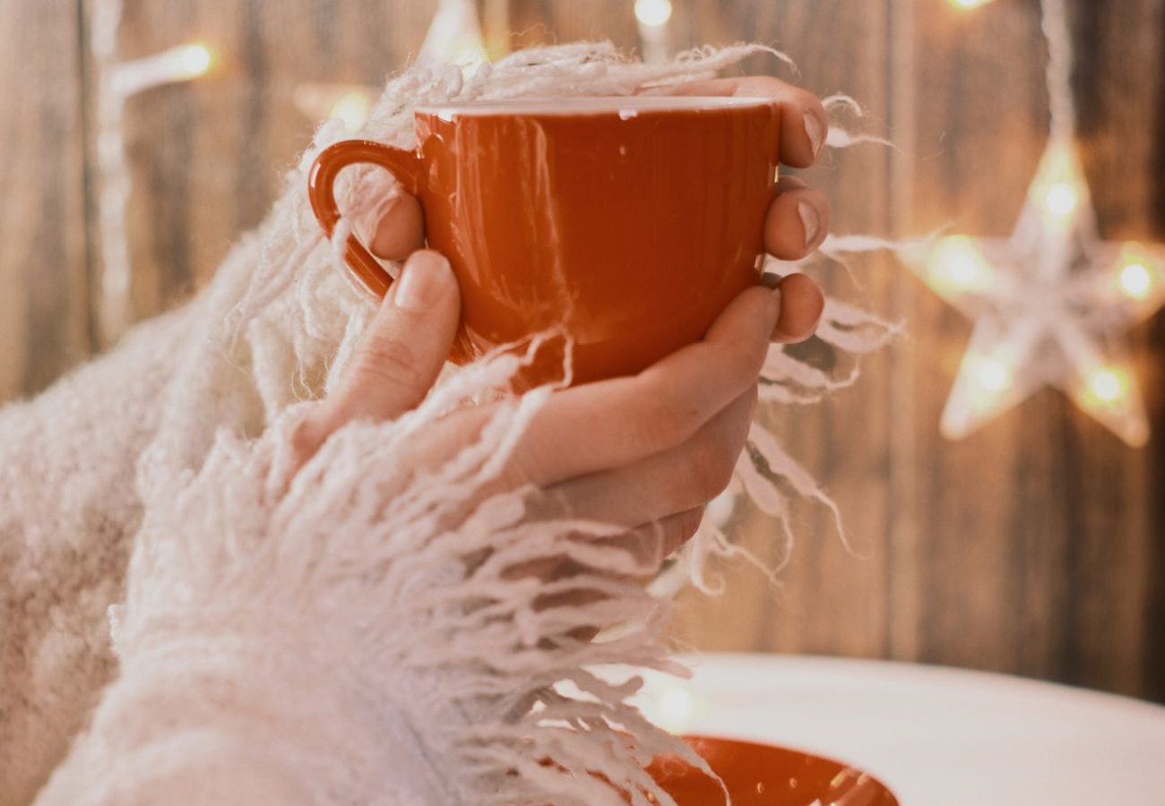 Hände halten eine warme Tasse in gemütlicher Adventsatmosphäre mit winterlicher Beleuchtung.